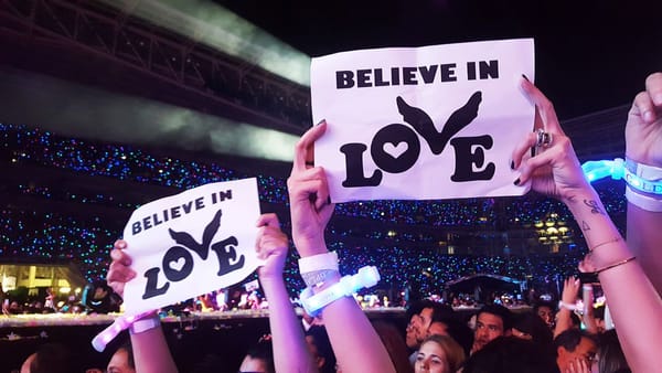 People holding a placard of "Believe in Love" in a Coldplay concert